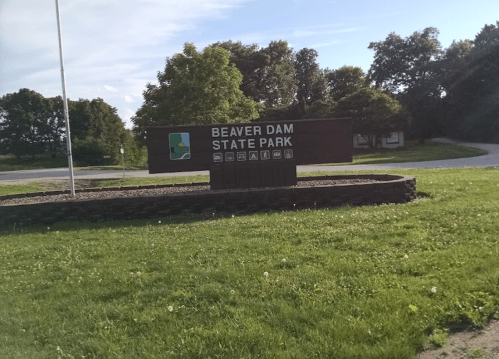 Sign for Beaver Dam State Park, surrounded by grass and trees, with a clear blue sky in the background.